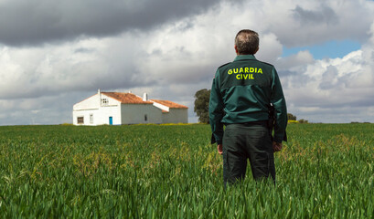 A Spanish civil guard watches over a country house from a grassy field.