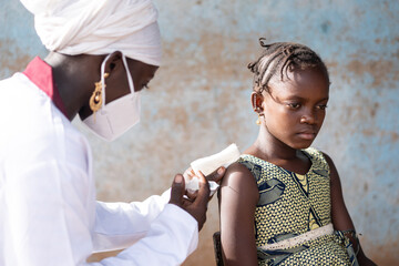 Young African nurse injecting a vaccine into the arm of a serious little black girl during an...