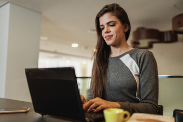 Young beautiful Brazilian woman working with laptop while sitting at office desk, working from home concept.