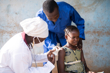 Worried little African schoolgirl during flu vaccination getting her intramuscular shot from a...