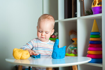 Toddler plays colorful plasticine play dough and copy space. Development of children from birth.