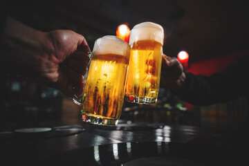 two glass of beer in hand. Beer glasses clinking in bar or pub - obrazy, fototapety, plakaty