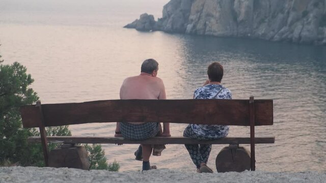 Elderly couple sitting together on a bench by the sea admiring the view