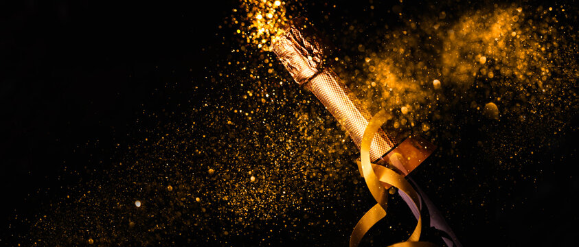 Luxury new year background. Champagne bottle with gold ribbon on dark background with golden bokeh glitter firework. Christmas celebration panoramic design banner.