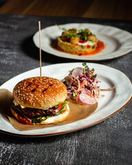 Fresh tasty burger with soft bun meat cutlet and fresh vegetables served with vegetable salad, White oval plate with whiskey on background. Vertical orientation