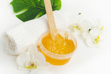 Sugar paste or wax honey in a transparent jar and white orchid on a white background. Sugaring....