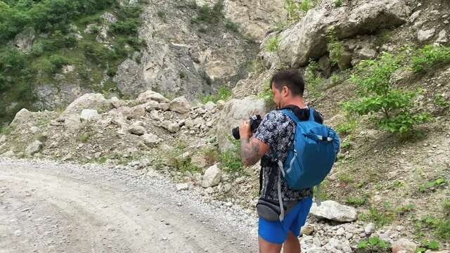 The guy takes pictures of the majestic nature of the Gizeldon Gorge with his camera. North Ossetia, Russia. Impenetrable rocks and majestic mountains. Summer landscape.