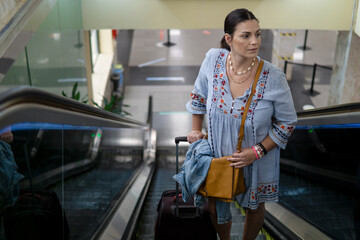 Beautiful Caucasian woman going up the escalator in the airport with a hand luggage