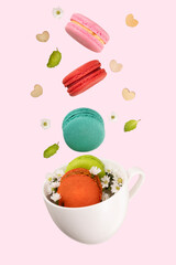 Colorful macarons, white little flowers, green mint leaf, amd wooden hearts floating on a white tea cup. Food levitation concepts.