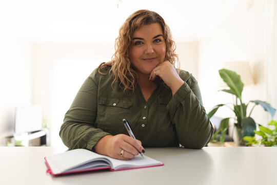 Portrait of caucasian woman having a video call, taking notes and smiling