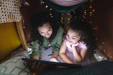 Happy mixed race mother and daughter using laptop in makeshift tent