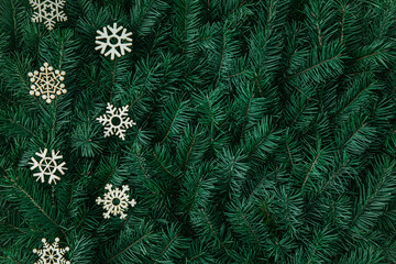 Natural fir tree branches texture with rustic wooden snowflakes. Dark green Christmas moody background. Winter pattern for Xmas decorations, ornament, noel cards. December festive backdrop, copy space
