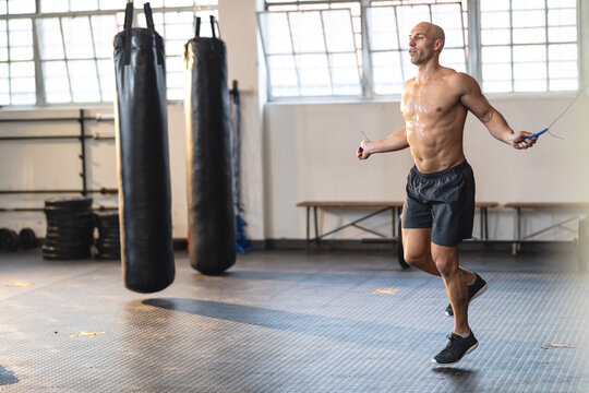 Strong caucasian man exercising at gym, holding rope and skipping