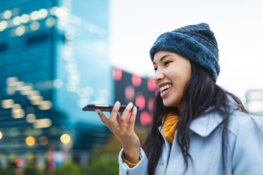Asian woman using smartphone and smiling in the street