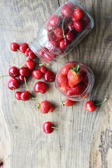Ripe strawberries and cherries , glass jars. Wood background, rustic style. The concept of making jam, homemade preparations