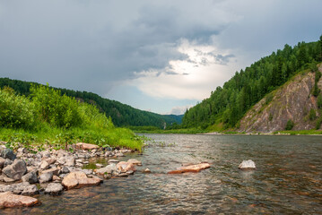 Landscape of Siberia. Kiya River, mountain banks and green forests in the Kemerovo region. Daytime landscape with blue skies and clouds.