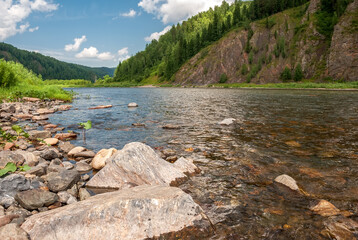 Landscape of Siberia. Kiya River, mountain banks and green forests in the Kemerovo region. Daytime landscape with blue skies and clouds.