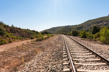 A ground-level view of a lonely train track crossing an inhospitable and arid landscape on a sunny morning.