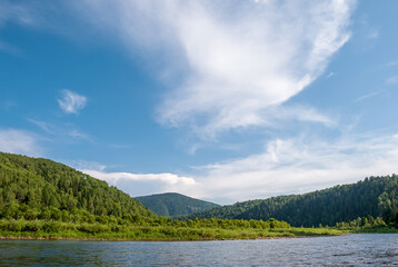 Landscape of Siberia. Kiya River, mountain banks and green forests in the Kemerovo region. Daytime landscape with blue skies and clouds.