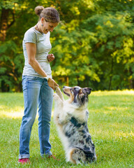 Vertical shot of playful mixed breed dog giving paw to happy middle aged woman while walking in...