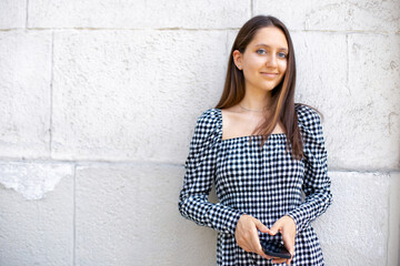 young attractive girl in a checkered dress holding a phone in her hands looking at the camera on a white isolated wall background