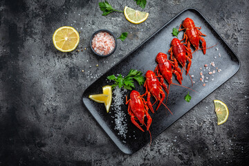 Boiled cooked crayfish crawfish with lemon and herbs on a slate plate ready to eat on black background. banner, menu, recipe place for text, top view