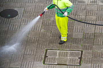 Worker holding a hose cleaning a sidewalk with water