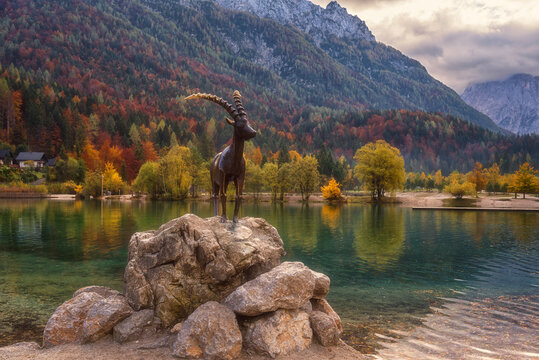 Kranjska Gora, Slovenia - October 18, 2019: Jasna lake in Triglav national park at sunrise, amazing autumn landscape with statue of Zlatorog, colorful trees and mountains, outdoor travel background