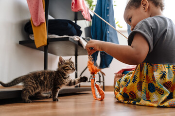 Black girl playing with kitten while sitting on floor © Drobot Dean