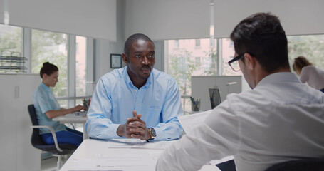 Fototapeta premium Back view of hr manager interview african male candidate sitting at desk in modern office