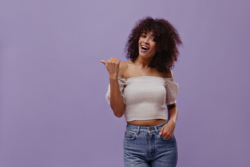 Excited dark-skinned woman points to left at place for text on purple background. Attractive lady...