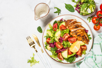Healthy salad with Grilled chicken fillet, fresh green leaves, avocado and vegetables. Top view at white background.