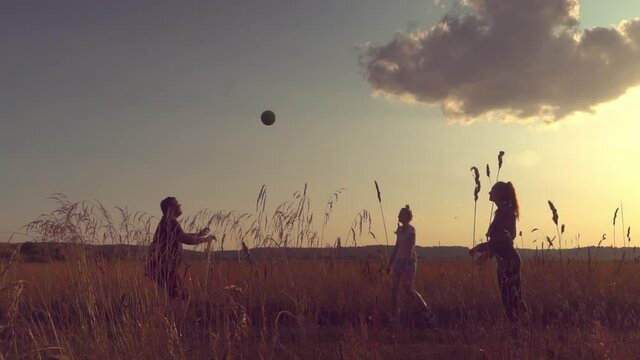 Three young energetic people are playing ball, volleyball at sunset on the field. Rural area, two girls and a guy. They have fun and have a great time. Youth and carelessness. slow motion,