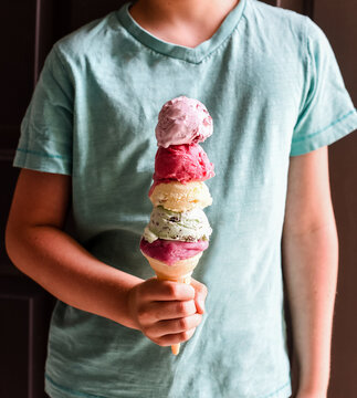 Close up of child's hand holding multi scoop ice cream cone.