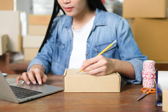 Online small business owner writing address on parcel box.