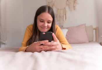 smiling girl lying on the bed with the smartphone