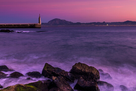 Waves Crashing on Playa Chica beach with statue of Sacred Heart of Jesus and Punta del Santo in distance, Tarifa, cadiz, Andalusia, Spain