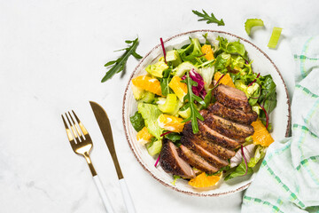 Salad with baked duck, green salad mix and oranges. Healthy food, diet meal. Top view at white marble table.