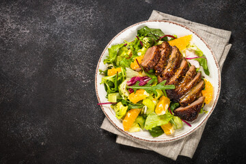 Salad with baked duck, green salad mix, oranges and honey mustard dressing. Healthy food, diet meal. Top view at black stone table.