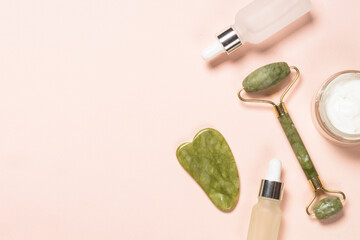 Face massage set. Jade roller and gua sha massager with serum bottles at pastel background. Anti-aging therapy. Top view with copy space.