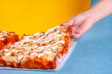 Hand lifting a squared slice from the Detroit style rectangular pizza with crusted cheese.
