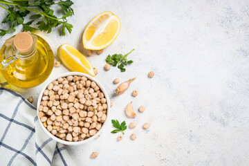 Chickpeas with ingredients for cooking hummus at light stone table. Top view with copy space.