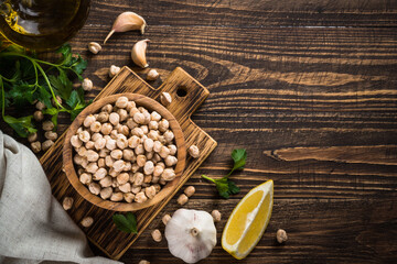 Chickpeas in a bowl with ingredients for cooking hummus at dark wooden table. Top view with copy space.