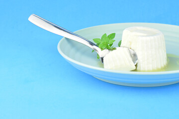 Fresh cheese with honey in circular plate on blue background.