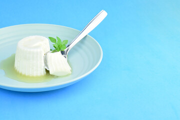 Fresh cheese with honey in circular plate on blue background. Copy space.