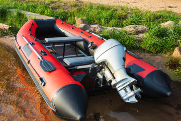 Red inflatable rubber boat with a motor near the lake shore, fishing, tourism, active recreation