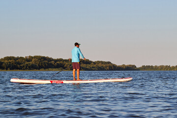 Man paddling on a big SUP board on a Danube river. Stand up paddle boarding - awesome active...