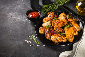 Grilled chicken wings with spices and tomato sauce at black kitchen table.