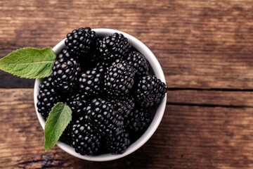 Blackberries in a white bowl with mint leaves on a wooden background close-up.