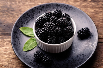 Fototapeta na wymiar Fresh blackberries in a white bowl on a black plate on a wooden background close-up.